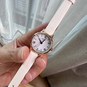 Close-up of gold watch case with white crocodile leather strap and Roman numerals