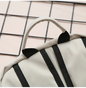 Detail view of reinforced black webbing handle stitching on beige minimalist canvas backpack