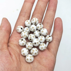 Detailed view of white acrylic round beads with golden star patterns held in hand