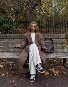 Detail of a brown double-breasted wool coat styled for fall in a scenic park setting