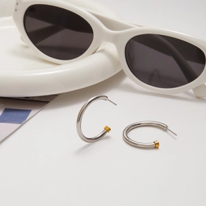 Detail of silver and gold two-tone C-shaped hoop earrings on a minimalist background
