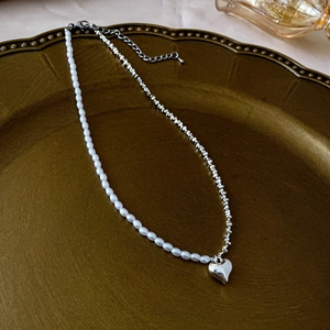 Detail of silver heart tassel necklace with pearl splicing on a vintage bronze tray