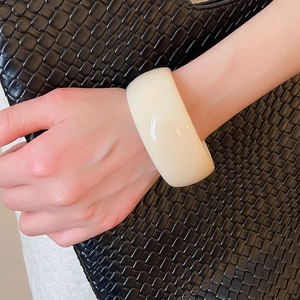 Close-up of a wide milky white resin bangle bracelet on a black woven leather handbag