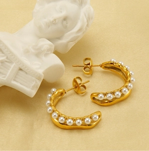 Détail de boucles d'oreilles dorées en C avec perles blanches et fermoirs papillon