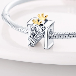 Detailed close-up of a silver letter M charm bead with zircons and gold crowns for DIY jewelry
