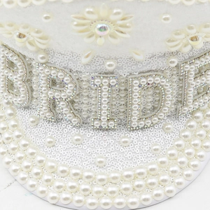 Detailed close-up of white bridal military hat with pearls, sequins and BRIDE lettering