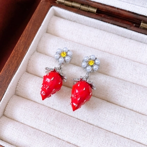 Macro detail of red strawberry earrings with pearls in a luxury wooden jewelry box