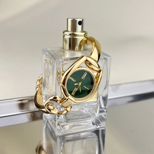 Detail of vintage gold bracelet watch with green dial wrapped around a glass perfume bottle