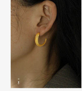 Close-up of a model wearing a textured gold C-shaped hoop earring with dotted finish