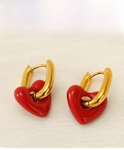 Detailed close-up of golden U-shaped earrings with glossy red heart-shaped pendants