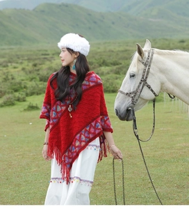 Ethnic knit poncho with red patterns and tassels worn by a model in a grassy field