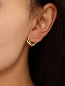 Macro close-up of a heart-shaped gold earring with colorful zircons on a model's ear