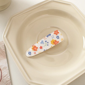 Detail of floral printed acrylic hair clip with colorful small blossoms on ceramic tray