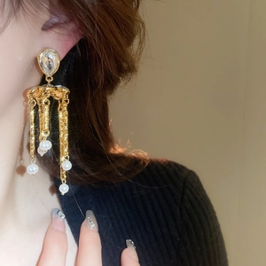 Détail de boucles d'oreilles à pompons dorés avec cristal, chaînes et perles blanches