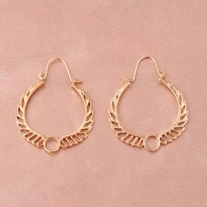 Close-up of golden hollowed wing earrings on a soft pink satin fabric background