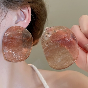 Close-up of irregular resin oval earrings in amber brown with elegant brushed texture