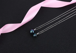 Detailed view of dual size black pearl pendants on silver chain over textured background
