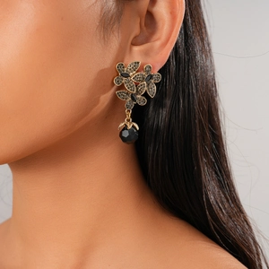 Detailed view of dark-style gold flower earrings with black crystals on a model