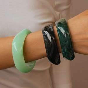 Detail of chunky resin bangles with green and ink marble patterns on female wrist
