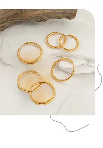 Close-up of three pairs of golden titanium steel hoop earrings on natural stone props
