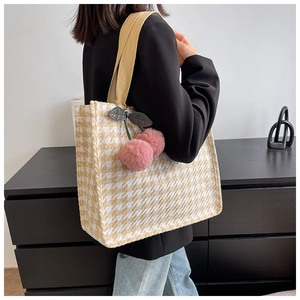 Detail of woven houndstooth tote bag featuring beige handles and a pink cherry charm