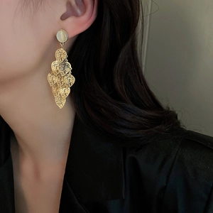 Close-up of golden long tassel earrings with hollow leaf design and opal stone on model