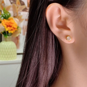 Close-up of golden hexagonal stud earring with clear zircon gem worn by a model