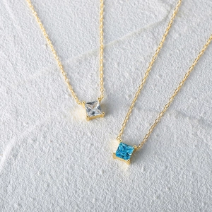 Detail of square claw-set zircon pendants in white and blue on gold chains