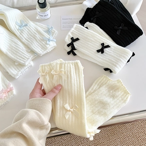 Détail de jambières en tricot côtelé avec des nœuds en satin blanc, noir et beige