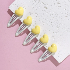 Detail showing five yellow heart hair clips on white metal bases over a pink surface