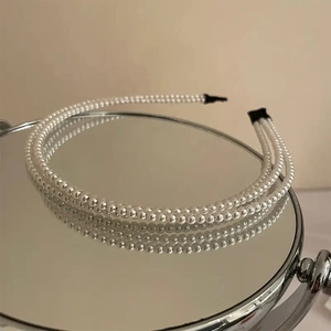 Detail view of a double-row pearl headband resting on a mirror with reflection