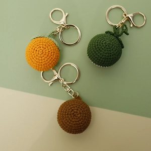 Handmade crochet fruit keychains featuring orange and green knit spheres with gold rings