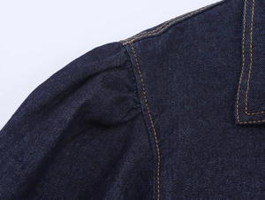 Dettaglio ravvicinato della giacca di jeans blu scuro con maniche a sbuffo e cuciture arancioni