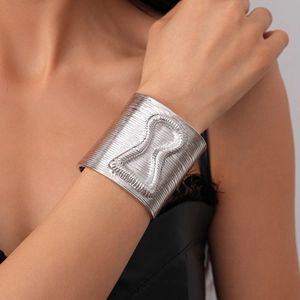 Macro detail of wide silver cuff bracelet showing fine linear textures and 3D hourglass relief