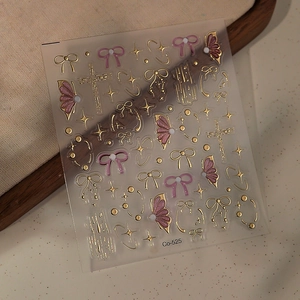 Detailed macro of 5D gold bow and star nail stickers with pink glitter on beige linen
