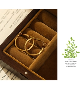 Macro shot of 18K gold plated hoop earrings in a wooden jewelry box with vintage paper