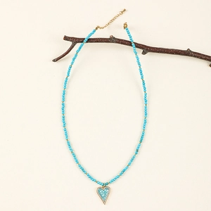 Detail of bohemian sky blue beaded heart necklace hanging on a rustic wooden branch