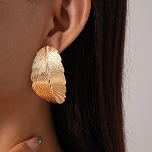 Close-up of oversized gold leaf earrings with textured veins worn by a model