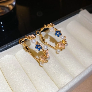 Detailed close-up of golden hoop earrings with enamel flowers and white pearls in a jewelry box