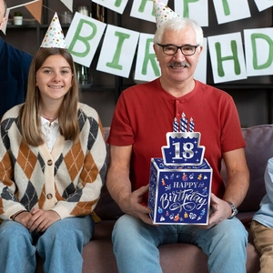 Hombre mayor sosteniendo caja azul marino para dinero de 18 cumpleaños en fiesta casera