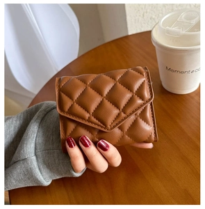 Close-up of a brown quilted leather wallet held by hand on a cozy wooden desk