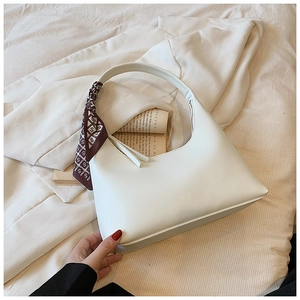 White crescent underarm bag with decorative printed silk scarf on soft beige fabric