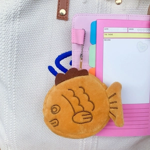 Detail of cute taiyaki plush coin purse with metal chain on canvas bag background