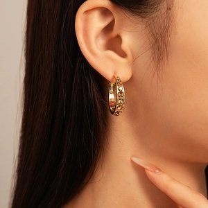 Detailed close-up of golden hoop earrings with brown crystals worn by a model