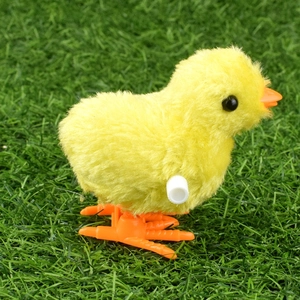 Close-up of wind-up yellow plush chicken toy with orange feet on green artificial grass