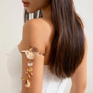 Close-up of golden floral arm cuff featuring polished ginkgo leaf tassels on a model