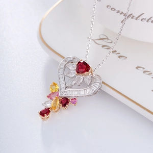 Macro shot of silver heart pendant featuring colorful gemstones on a white porcelain dish