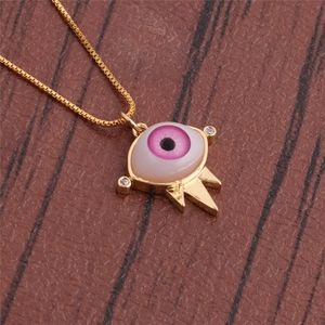 Macro detail of gold evil eye pendant with pink resin eye and cubic zirconia accents