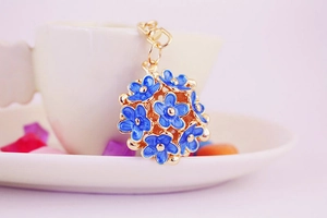Detail of blue enamel flower keychain with gold metal lobster clasp on a white cup