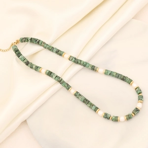 Close-up of green natural stone and pearl necklace on beige silk and white plate